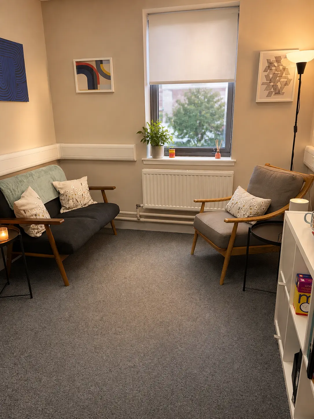 A softly lit counselling room with a linen armchair, plant and a warm mug